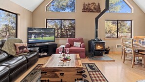 A spacious living room with a large TV, a fireplace, and a cozy seating area. - High Country Escape | Forest Border • Fenced Yard (Heber)