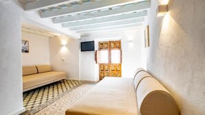A room with a sofa, a television, a patterned floor, and a wooden door. - Bekkeh Posada Boutique (Vejer de la Frontera)