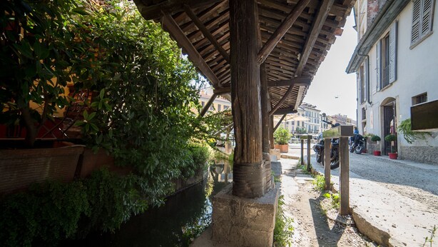 A covered outdoor area with a stone bench, a narrow water channel, and a cobblestone path. - HbHall - Navigli 2 Apartment  (Milan)