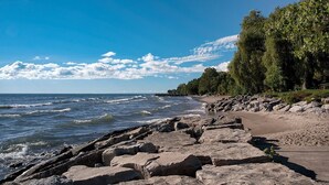 A rocky shoreline with waves, a clear sky, and trees.