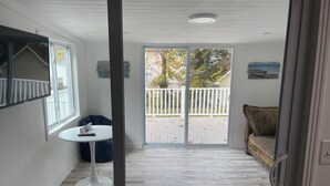 A room with a white ceiling, a round white table, a blue bean bag, a patterned sofa, and a view of a white fence and trees through a sliding glass door.