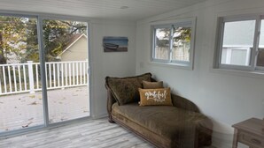 A room with a sliding glass door leading to a deck, a brown sofa with a 'grateful' pillow, and a small wooden table.
