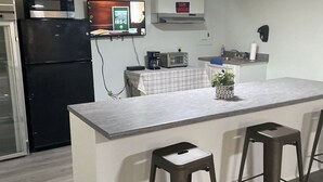A modern kitchen with a central island, bar stools, a refrigerator, a microwave, a coffee maker, and a TV mounted on the wall. - Promised Land Countryside Getaway/Campsite  (Bradley)