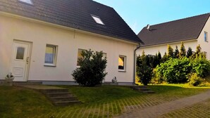 Ein zweistöckiges Haus mit geneigtem Dach, einer Haustür und einem kleinen Fenster. Ein gepflasterter Weg führt zur Haustür.