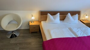 Ein Schlafzimmer mit einem Bett, zwei Nachttischen mit Lampen, einem hölzernen Kopfteil, einem Sessel und Holzboden.