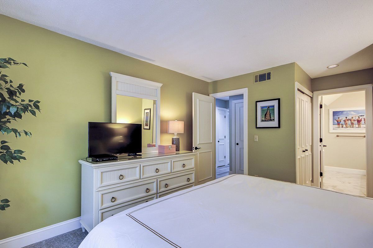 Une chambre à coucher comprenant un lit, une commode, un téléviseur et une porte donnant sur une autre pièce.