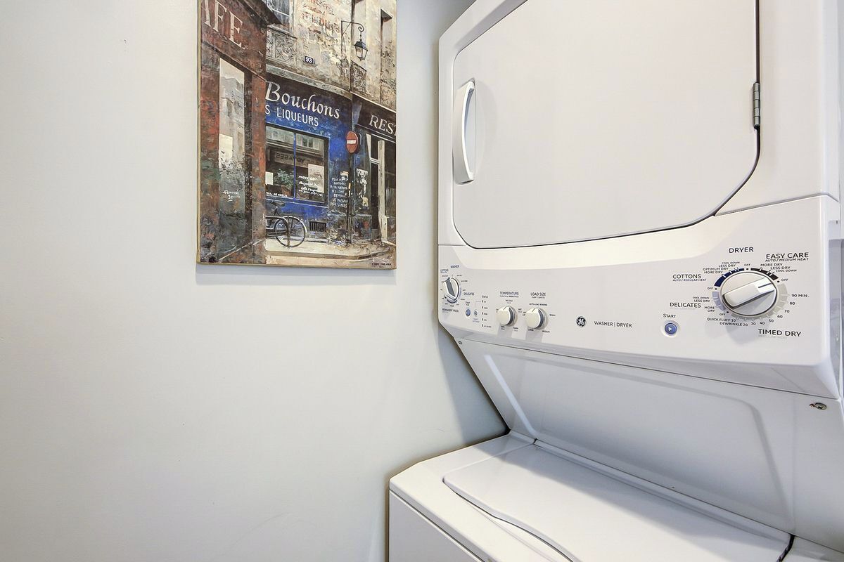 A front-loading washing machine with a control panel, a wall-mounted poster of a street scene, and a white wall.