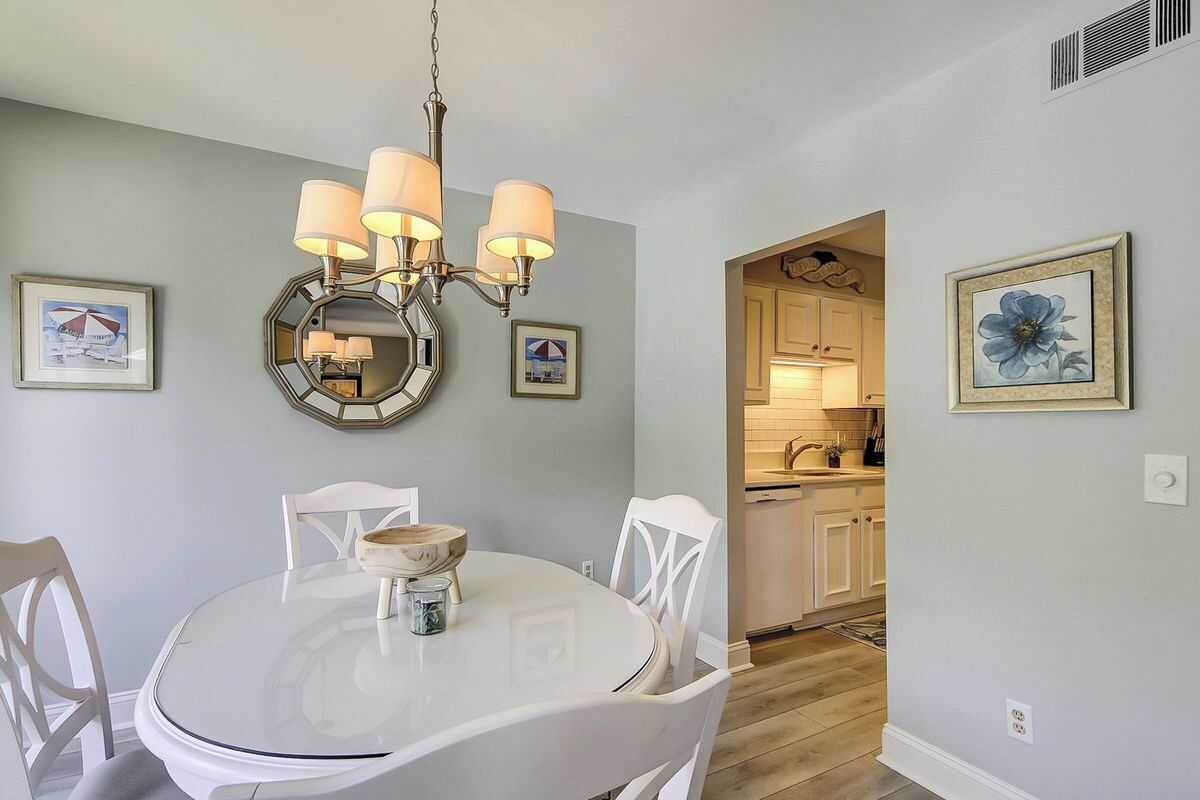 A dining area with a round table, white chairs, a chandelier, and framed artwork on the walls.