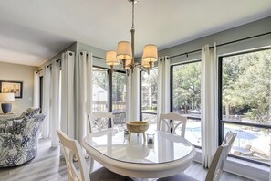 Un espace repas comprenant une table ronde, des chaises, un lustre et de grandes fenêtres avec des rideaux.