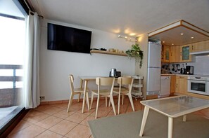 A compact living space with a dining area, kitchenette, and a TV mounted on the wall.