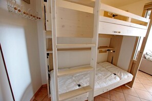 Un lit superposé à trois niveaux, avec des étagères en bois et un petit bureau.