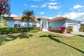 A two-story house with a well-maintained lawn, a palm tree, and various shrubs.