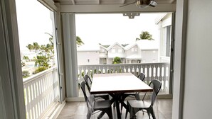 A balcony with a table and chairs, a ceiling fan, and a view of houses and palm trees. - Éden love! (Collectivité de Saint-Martin)