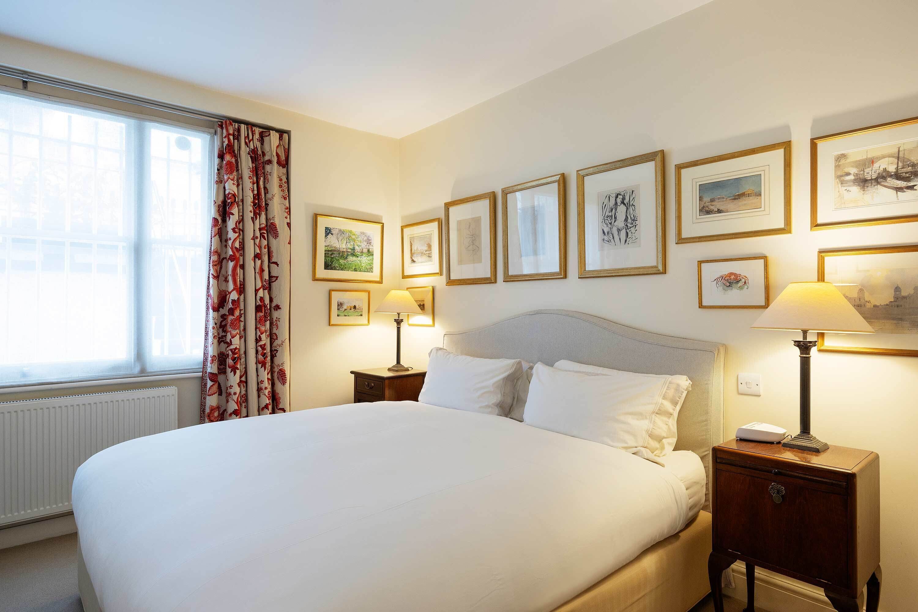 A neatly made bed with white linens, a nightstand with a lamp, and framed artwork on the wall.