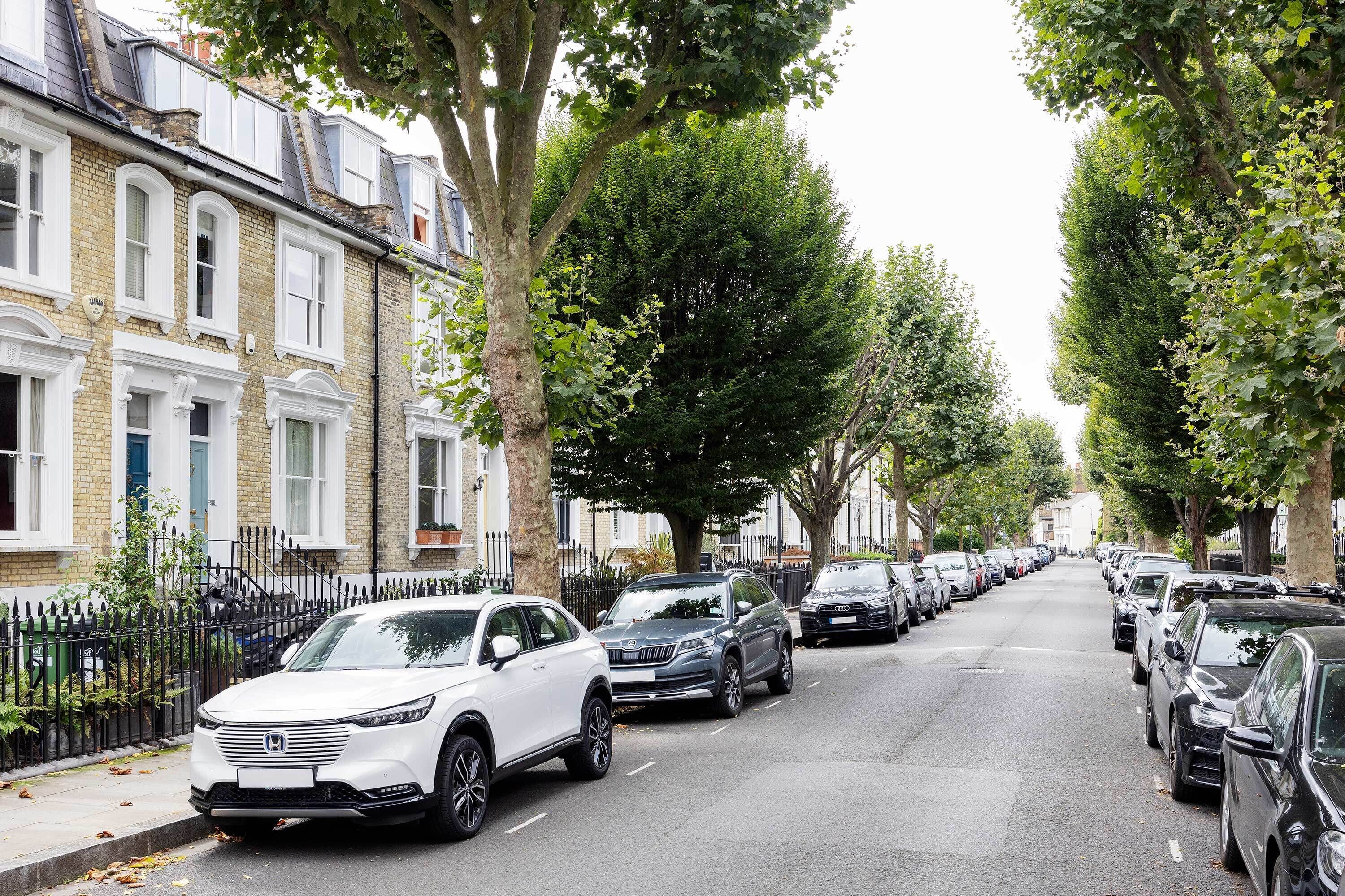 Une rangée de voitures garées le long d’une rue bordée d’arbres, avec des immeubles d’habitation d’un côté.