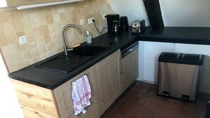 Una cocina con encimera negra, armarios de madera, pileta de acero inoxidable y un bote de basura.