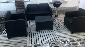 Un patio con mobiliario exterior, incluyendo un sofá, dos sillones y un pequeño otoman.