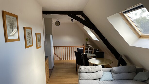 Un loft moderno con piso de madera, un sofá gris, una mesa de madera y una cocina al fondo.