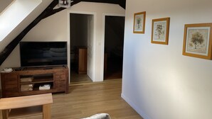 Una habitación con techo inclinado, muebles de madera, un televisor de pantalla plana e impresiones botánicas enmarcadas en la pared.
