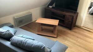 Una sala de estar con un sofá gris, una mesa de centro de madera, un televisor sobre un mueble de madera y un radiador.