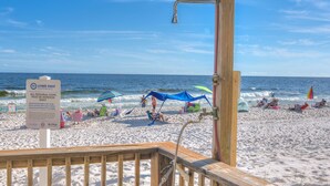 A beach with a wooden deck, a sign indicating personal items must be removed daily, and beach umbrellas. - Tropical Winds 603 2 Bedroom Condo by RedAwning (Gulf Shores)