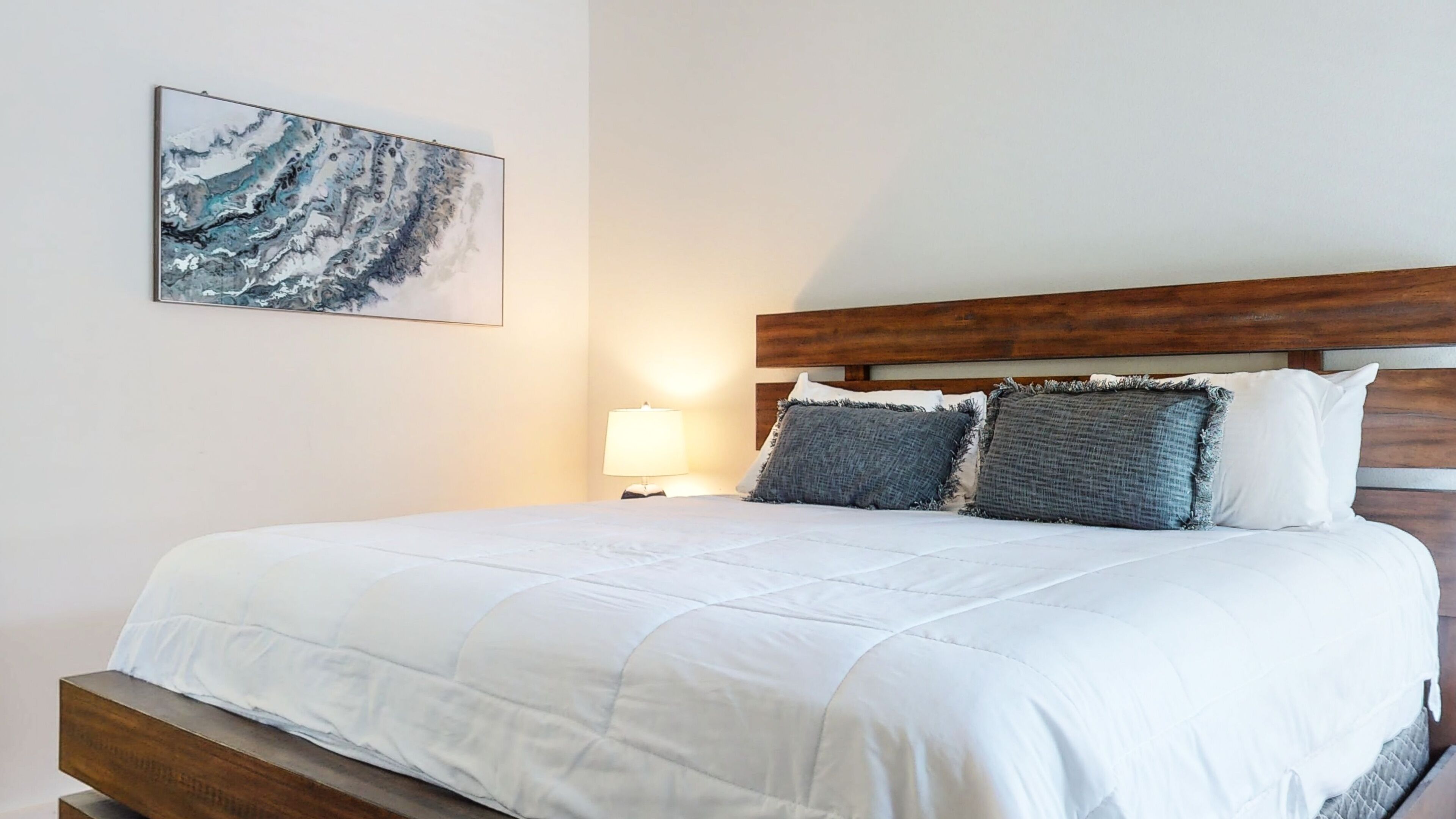 A neatly made bed with a white duvet, a wooden headboard, and three pillows.