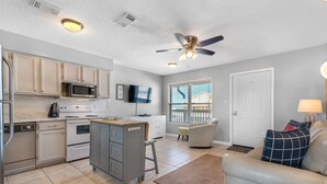 A kitchen with white cabinets, a microwave, and a stove. There is a ceiling fan and a window with blinds. - Lagoon Landing 305 1 Bedroom Condo by RedAwning (Gulf Shores)