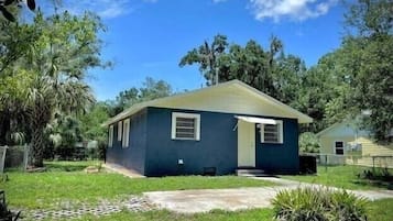 A small, single-story house with a dark blue exterior, a front porch, and a well-maintained lawn.