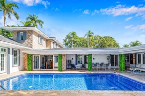Une maison moderne dotée d’une piscine, de mobilier de jardin et de palmiers.