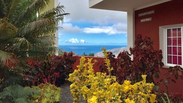 A hotel entrance with a view of the sea, surrounded by tropical plants and a red building with a sign reading "MATERNOS CATALINO". - Catalina 4 (El Paso)