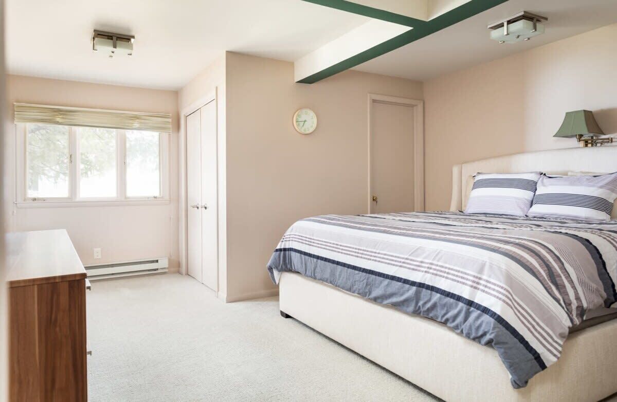 A bedroom with a bed, a bedside table, a lamp, and a window with blinds.