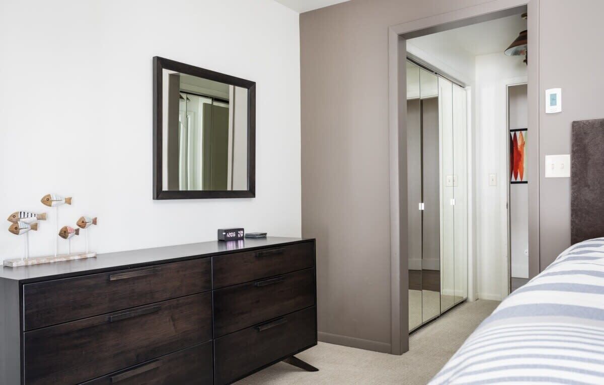 A bedroom with a dark wooden dresser, a mirror, and a bed with striped bedding.