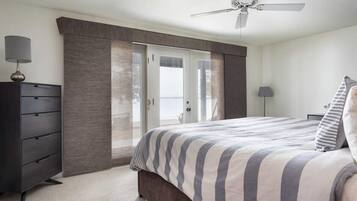 A bedroom with a bed, a dresser, a ceiling fan, and a door leading to a balcony.