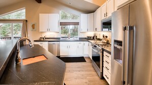 Una cocina moderna con armarios blancos, electrodomésticos de acero inoxidable y un amplio ventanal que proporciona luz natural.