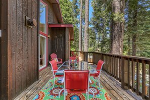 Une terrasse en bois avec une table en verre et des chaises rouges, entourée de grands arbres.