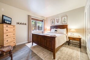Une chambre à coucher avec un lit en bois, une commode en bois, une chaise, une fenêtre avec des rideaux et des œuvres d’art accrochées au mur.
