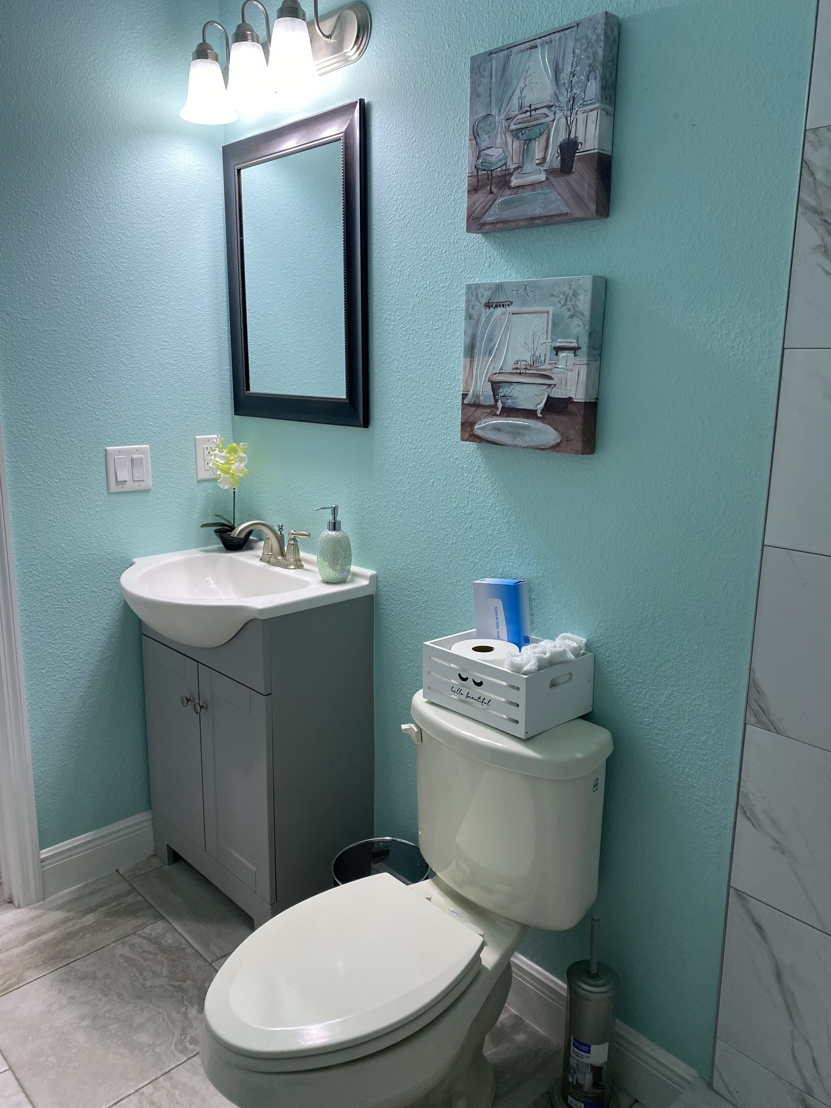 Un baño con inodoro, lavamanos y tocador. Hay luces empotradas en la pared, un espejo y dos cuadros enmarcados.