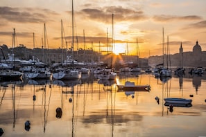 Un puerto deportivo al atardecer con varias embarcaciones amarradas, agua tranquila y un edificio histórico al fondo.