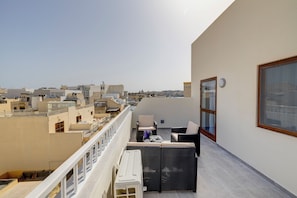A rooftop terrace with a view of the cityscape, furnished with outdoor seating and a railing.