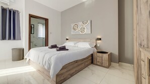 Un dormitorio moderno con una cama de madera, una mesita de noche pequeña, una obra de arte en la pared y una puerta de cristal que da al baño.