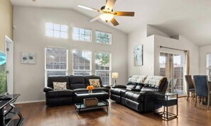 A spacious living room with a black leather sofa, a coffee table, and a dining area with chairs and a table.