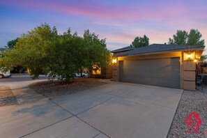 A residential garage with a driveway, surrounded by trees and a clear sky.