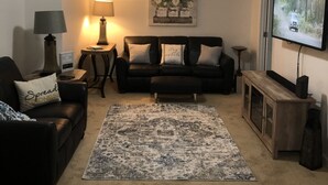 Ein Wohnzimmer mit schwarzem Ledersofa, einem Couchtisch, einem Fernseher und einem Bild an der Wand.