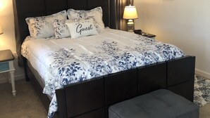 Ein Schlafzimmer mit einem dunklen Holzbett, floralem Bettzeug, einer Bank, einem Nachttisch und einer Lampe.