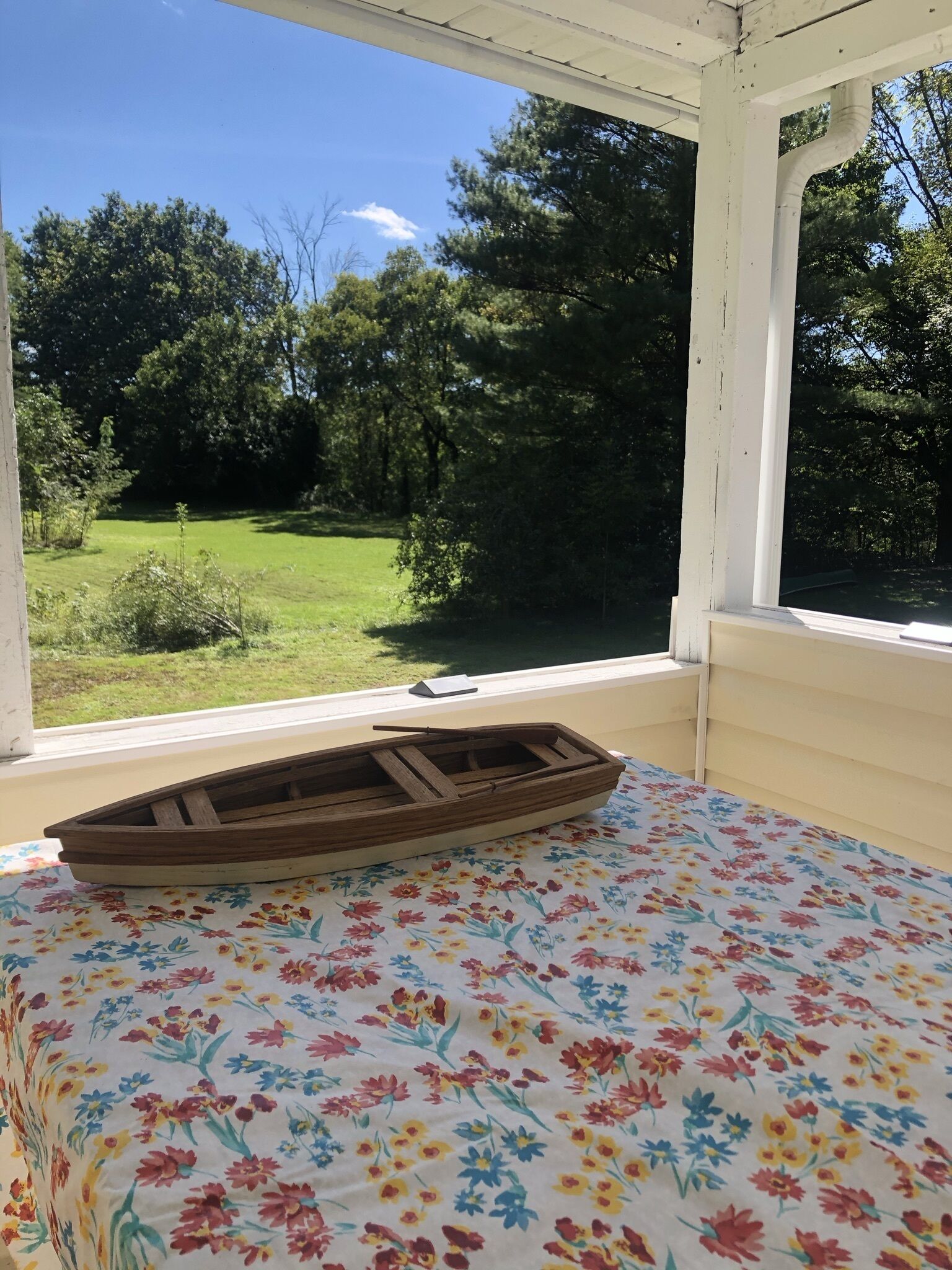 A room with a bed, a wooden boat on the bed, and a view of a green landscape through a window.