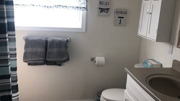 Une salle de bain comprenant des toilettes, un lavabo et un meuble de rangement, une fenêtre avec un rideau et deux serviettes accrochées au mur.