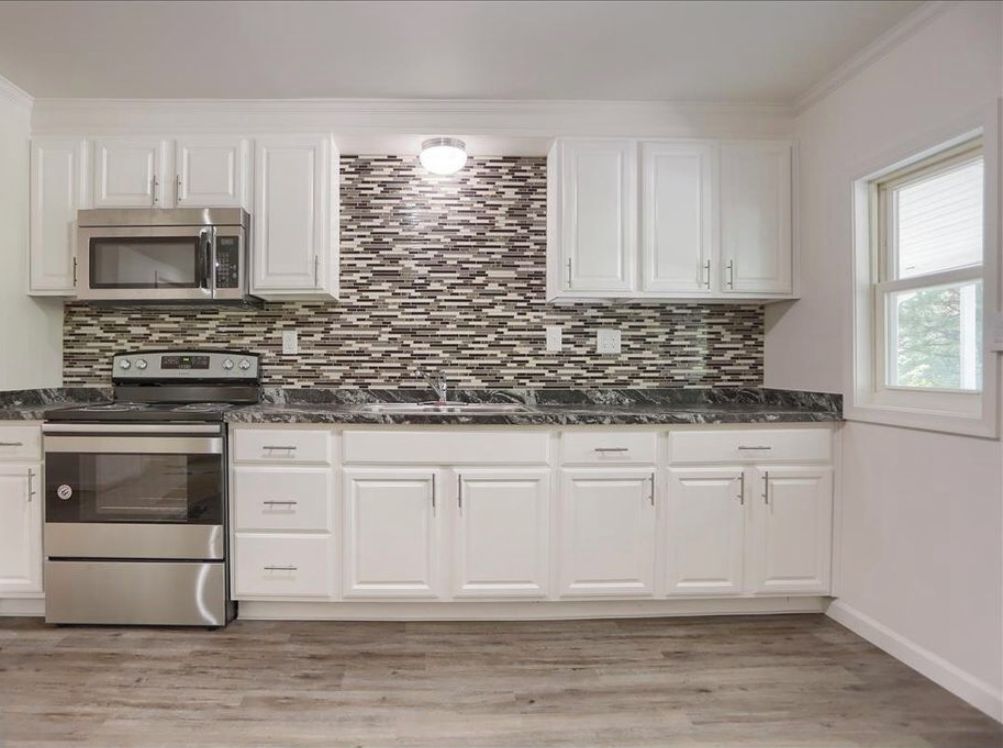 A kitchen with white cabinets, a stainless steel microwave, a built-in oven, and a patterned backsplash.
