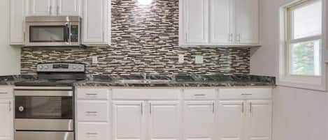 A kitchen with white cabinets, a stainless steel microwave, a built-in oven, and a patterned backsplash.