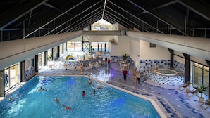 Ein Hallenbad mit mehreren Bahnen, einem Sprungbecken und einer Sitzgelegenheit mit Stühlen und Pflanzen in Töpfen.