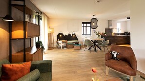 A modern living room with a sofa, a dining area with a table and chairs, and a kitchen in the background.